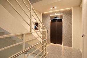 A modern elevator with a digital display, a glass staircase with metal railings, and a textured wall. - Nori Hotel (Seoul)