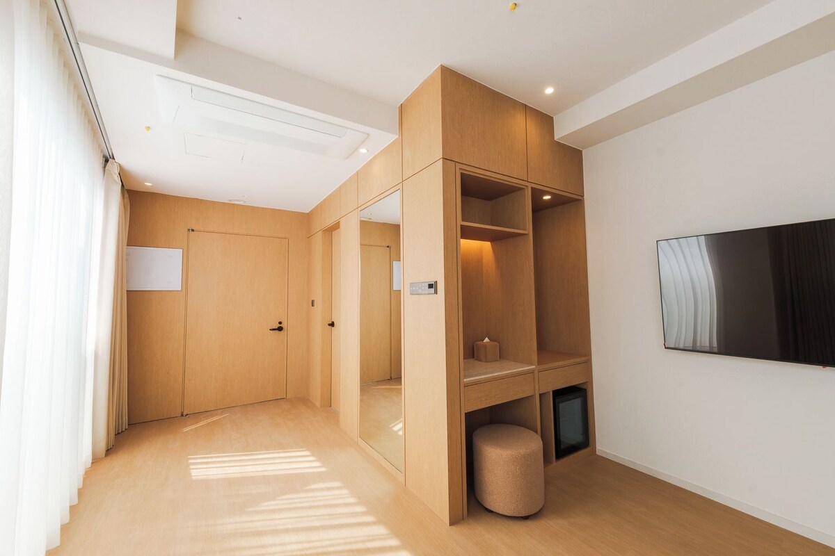 A modern room with a wooden wardrobe, a television mounted on the wall, and a small round stool.