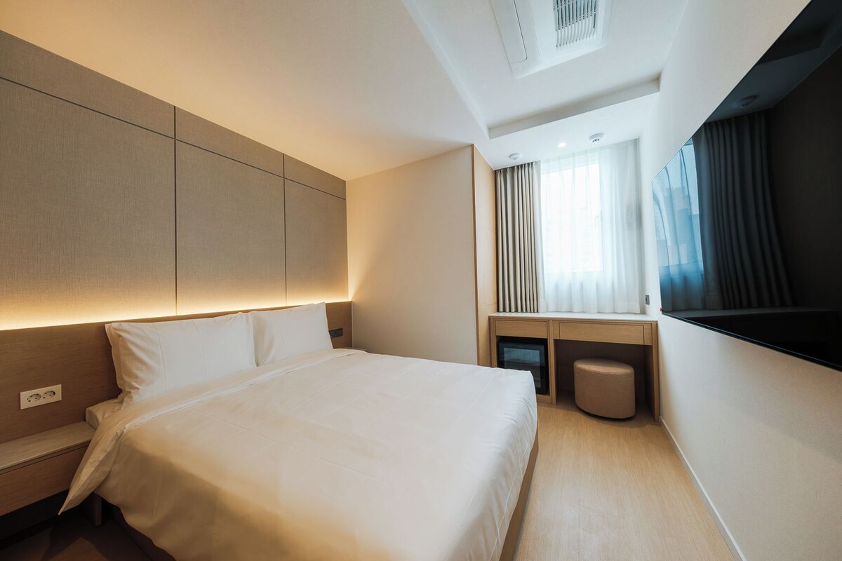 A modern hotel room with a large bed, a desk, and a window with curtains.