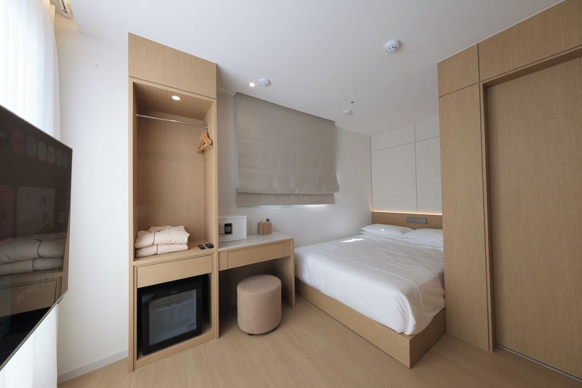 A modern hotel room with a bed, a desk, a wardrobe, and a television.