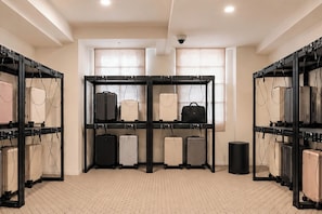A room with a tiled floor, a black luggage rack with suitcases, a radiator, and a security camera on the ceiling. - Nori Hotel (Seoul)