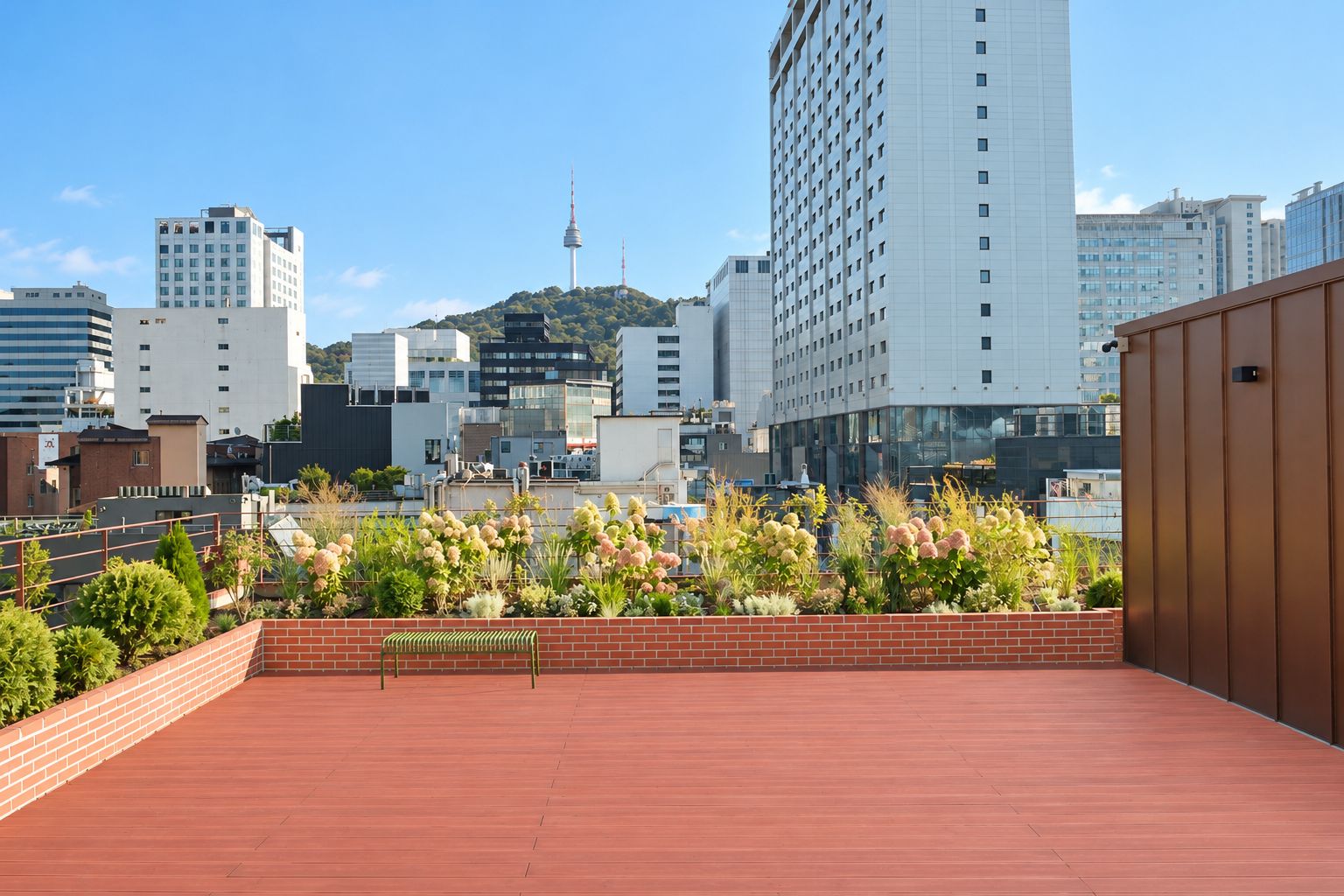 Une terrasse sur le toit, avec un mur en briques et une plateforme en bois, offrant une vue sur un paysage urbain composé d’immeubles modernes et d’une colline surmontée d’une tour.