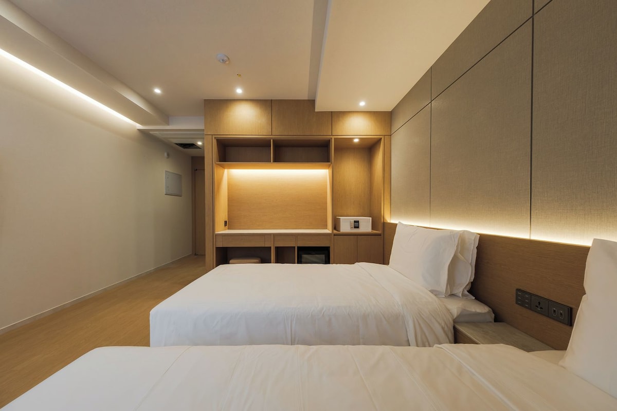 A modern hotel room with two beds, built-in shelving, and recessed lighting.