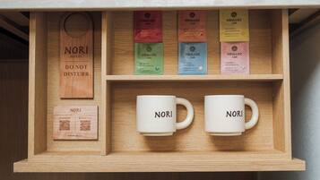Una caja de madera con bolsitas de té y dos tazas blancas con la etiqueta 'NORI HOTEL', junto a un letrero de madera que dice 'NO MOLESTAR'.