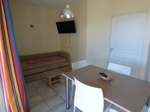 A room with a bed, a table, chairs, a television mounted on the wall, and a door.