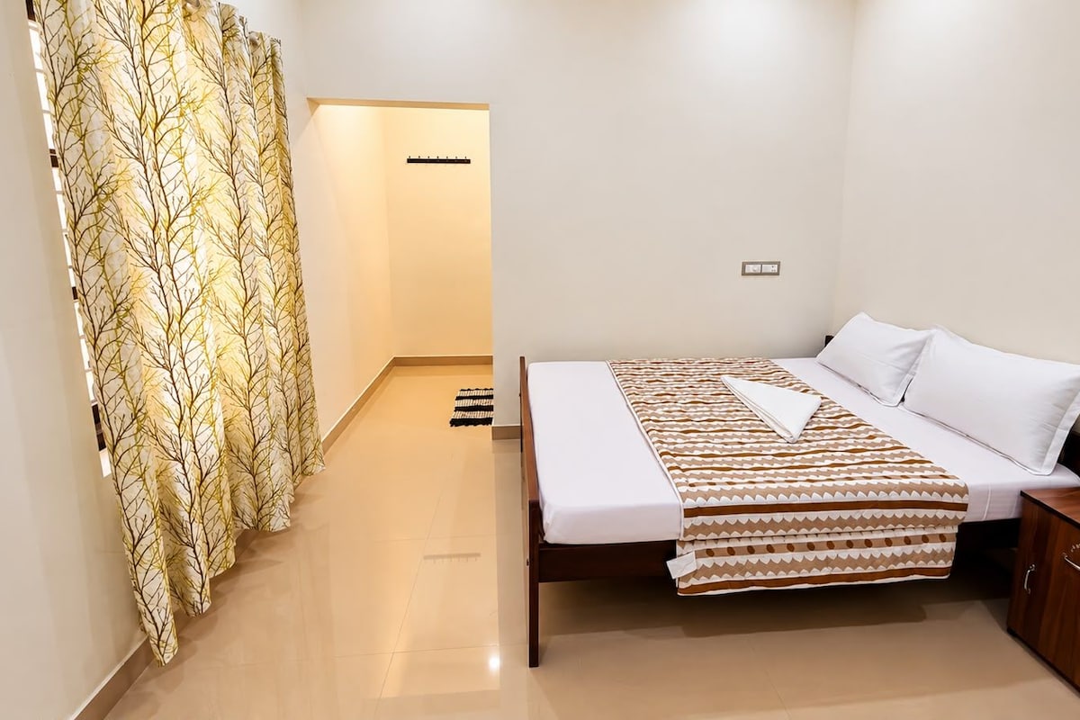 A hotel room with a bed, bedside table, and a curtain with a tree pattern.