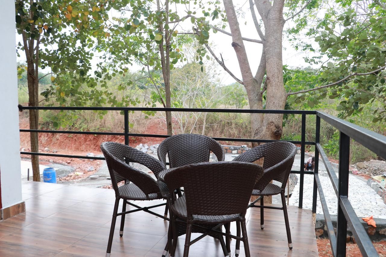 Un área de estar al aire libre con sillas de mimbre y una mesa, rodeada por una barandilla con vistas a árboles y un paisaje natural.