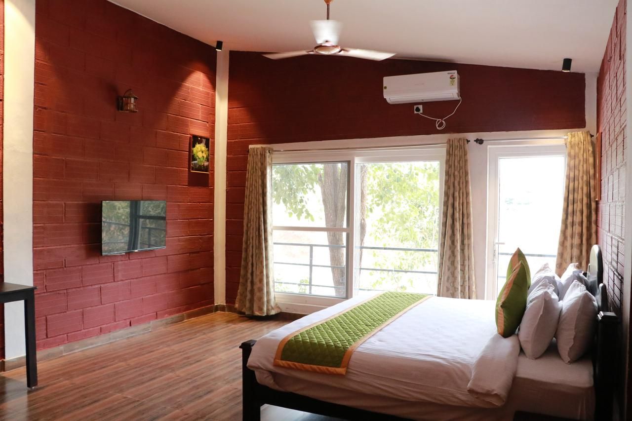 A bedroom with a bed, a ceiling fan, an air conditioning unit, a window with curtains, and a brick wall.
