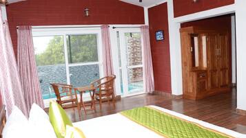A room with a bed, a table with chairs, a wooden wardrobe, and a view of the sea through a glass door.
