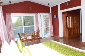 A room with a bed, a table with chairs, a wooden wardrobe, and a view of the sea through a glass door.