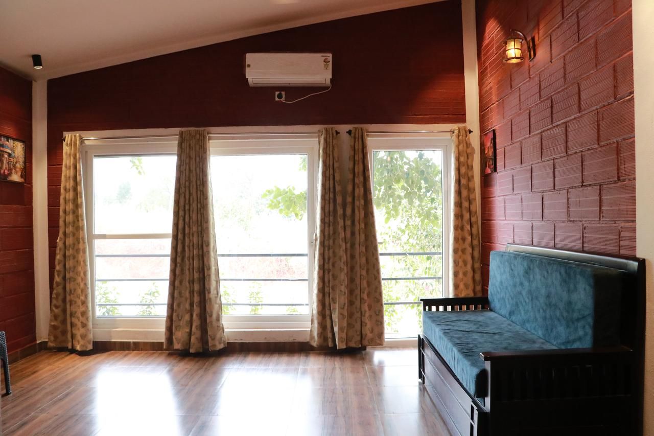 A room with a wooden floor, a blue sofa, a window with curtains, and a brick wall.