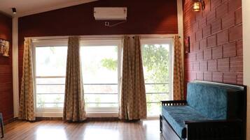 A room with a wooden floor, a blue sofa, a window with curtains, and a brick wall.