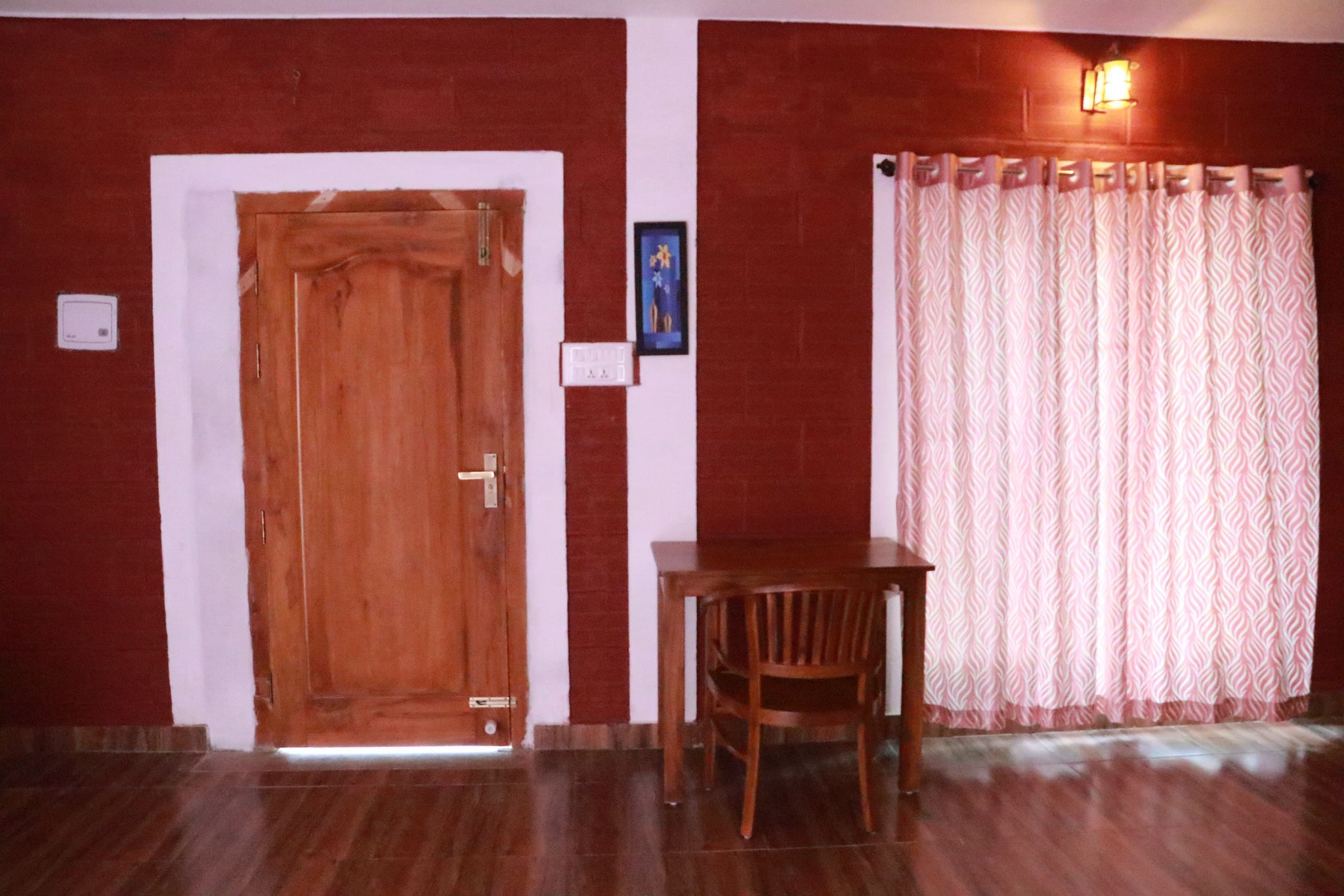 Una habitación con puerta de madera, una mesa pequeña con una silla y un cortinaje con diseño ondulado.