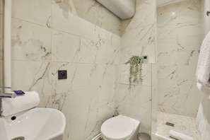 Une salle de bain avec un sol en marbre blanc, des toilettes blanches, un lavabo et un espace douche.