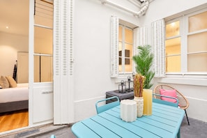 Une pièce avec une table bleue, des chaises blanches, une plante en pot et un lit avec des oreillers.