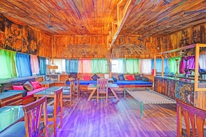 A rustic interior with wooden walls and ceilings, a central seating area with cushions, and a colorful window treatment.
