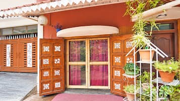 Una puerta de madera con elaborados diseños blancos, un felpudo rojo en la entrada y una planta en maceta sobre un soporte de metal blanco.