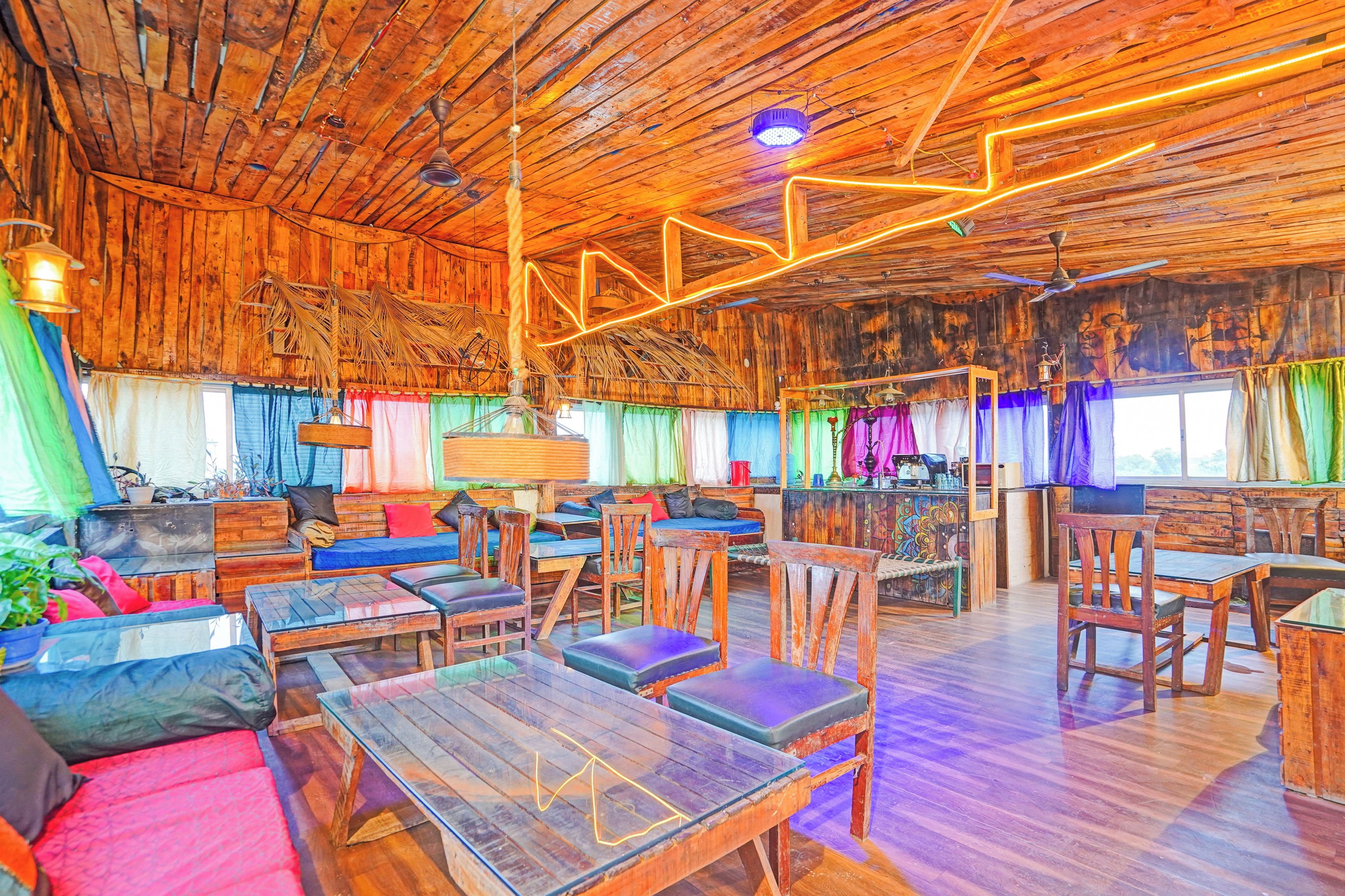 Interior rústico em madeira, com teto alto, mobiliário de madeira e cortinas coloridas.