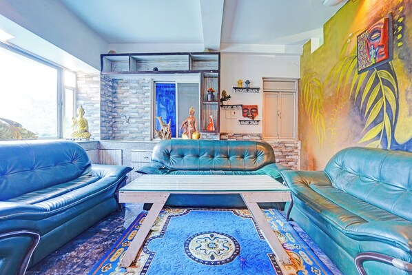 A living room with blue leather sofas, a coffee table, a patterned rug, and a stone wall.
