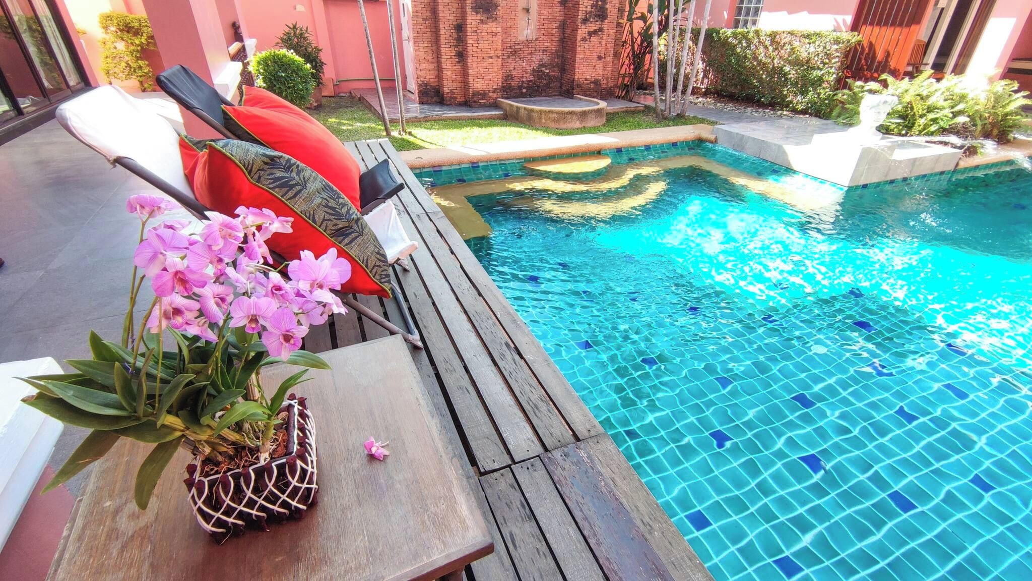 A pool area with a wooden deck, lounge chairs, and a potted orchid.