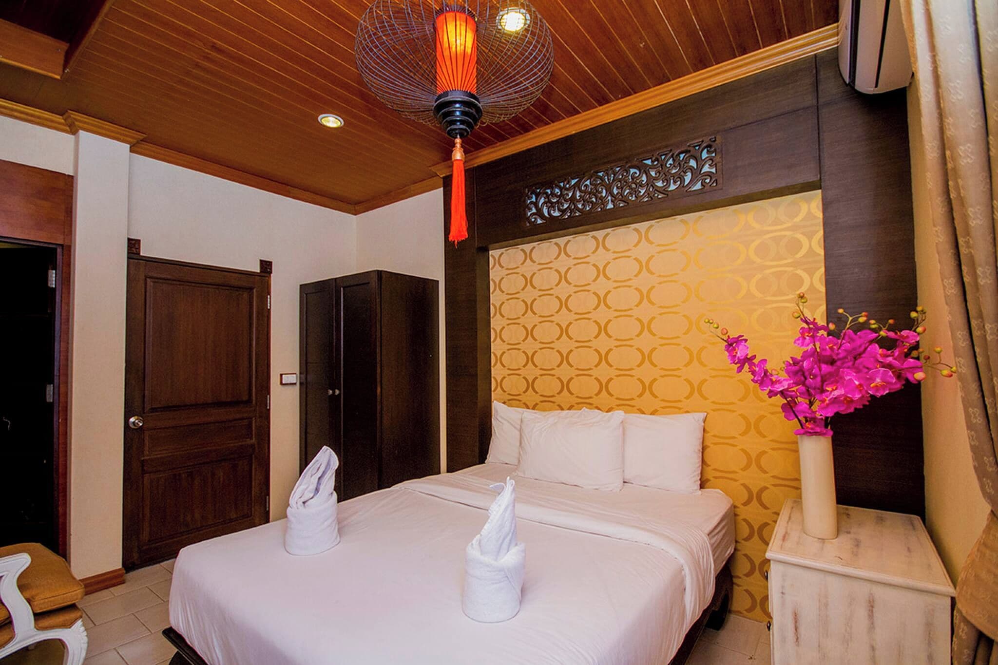 A hotel room with a bed, a nightstand, a vase with flowers, a door, and a ceiling light fixture.