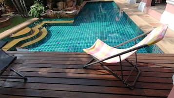 A pool area with a wooden deck, a checkered lounge chair, and a tiled pool.