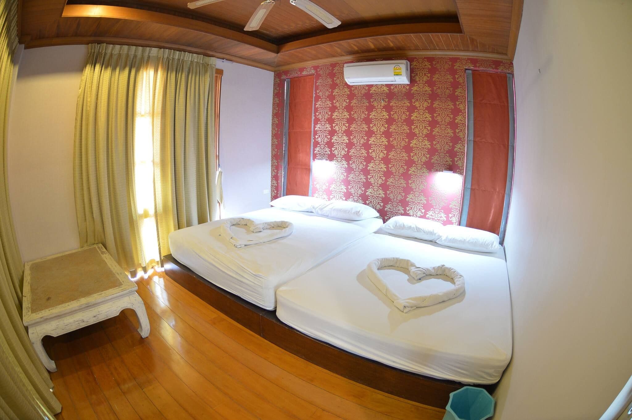 A hotel room with two beds, a wooden floor, a small table, and a ceiling fan.