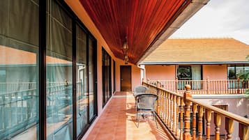 A covered outdoor balcony with a wooden railing, a chair, and a view of a building with large windows.