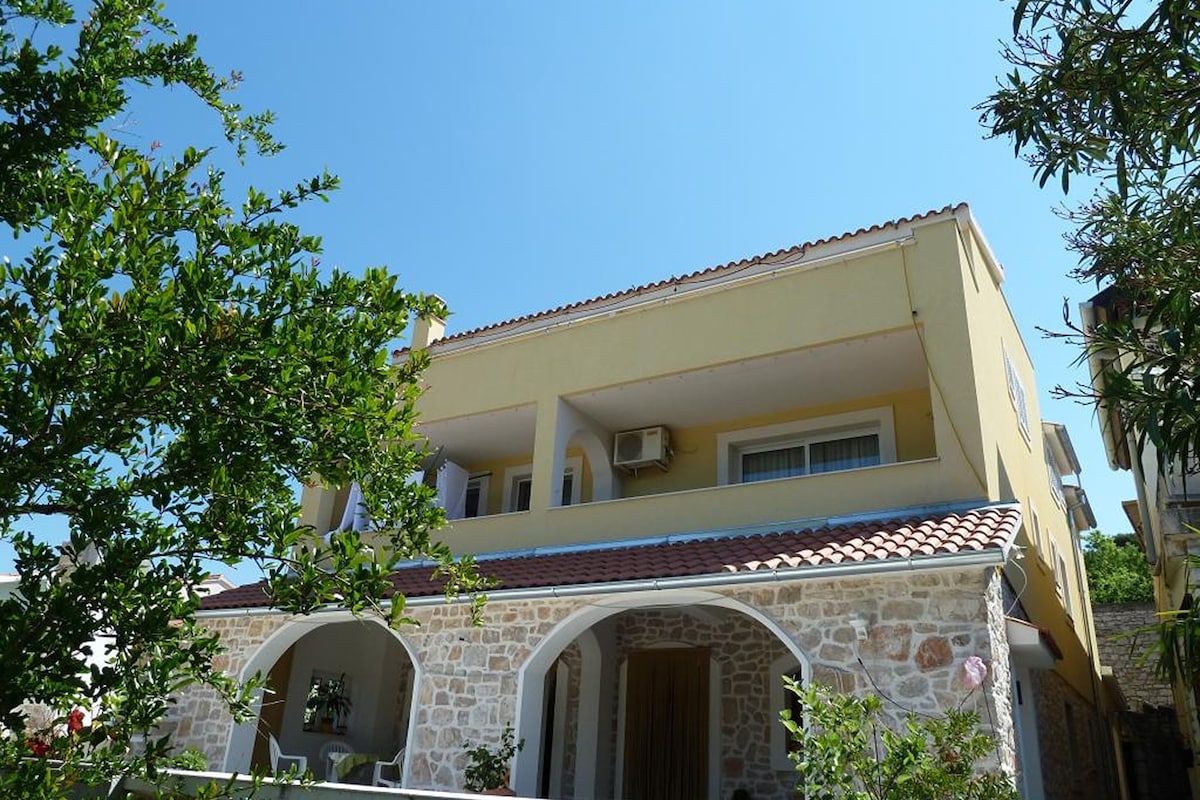 A two-story building with a stone facade, a tiled roof, and a clear blue sky.