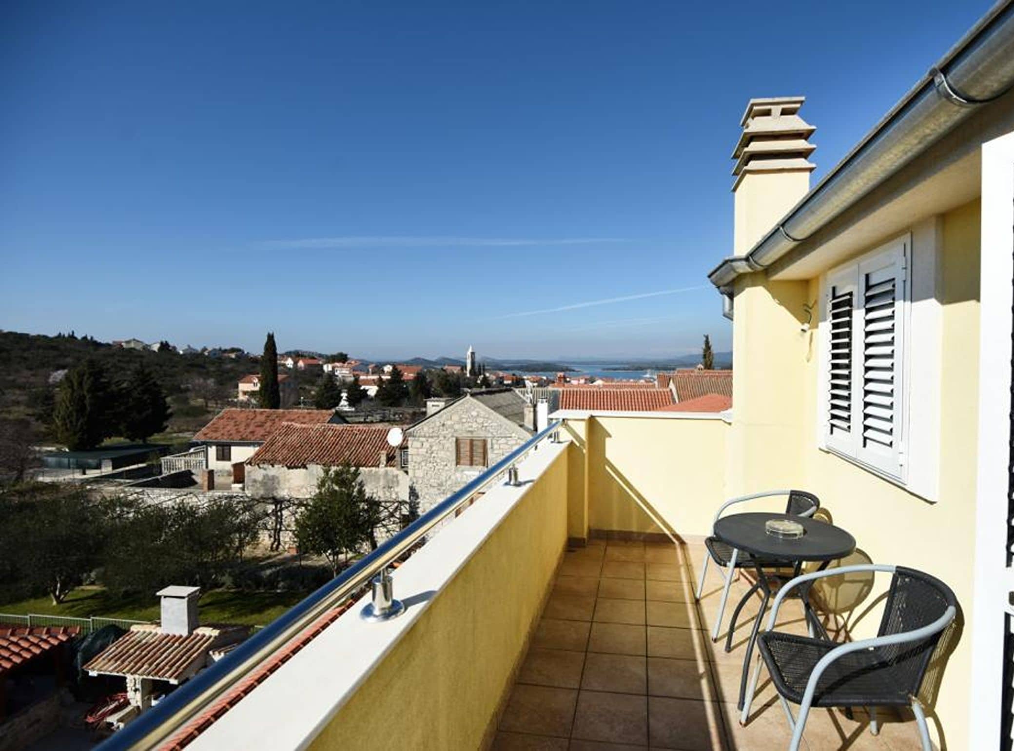 A balcony with a view of a town, a table, and two chairs.