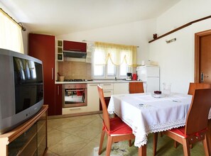 Eine kleine Küche mit Fernseher, Esstisch, Stühlen und Kühlschrank.