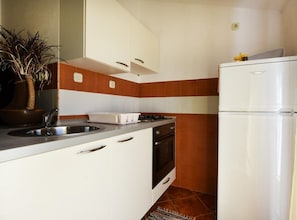 A compact kitchen with white cabinets, a stove, a sink, and a white refrigerator. - Apartments Milena (Murter-Kornati)