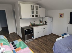 Cocina compacta con armarios blancos, horno empotrado, refrigerador y lavaplatos.