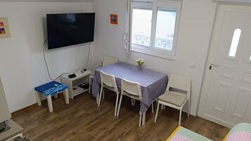 Una habitación con una televisión montada en la pared, una mesa de comedor con sillas, una ventana con vistas y una puerta.