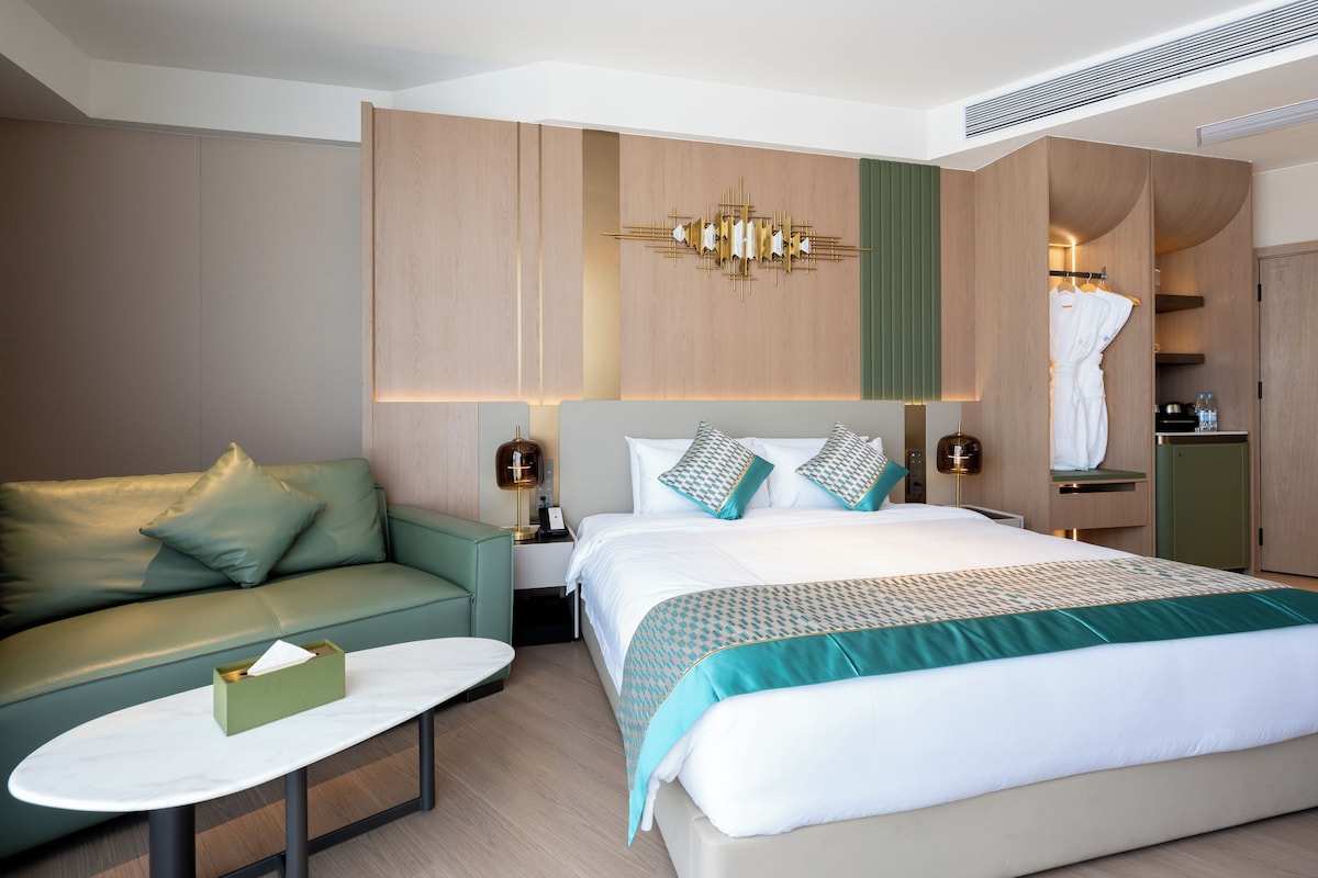 Habitación de hotel moderna con una cama grande, un sofá, una mesita y un vestidor.