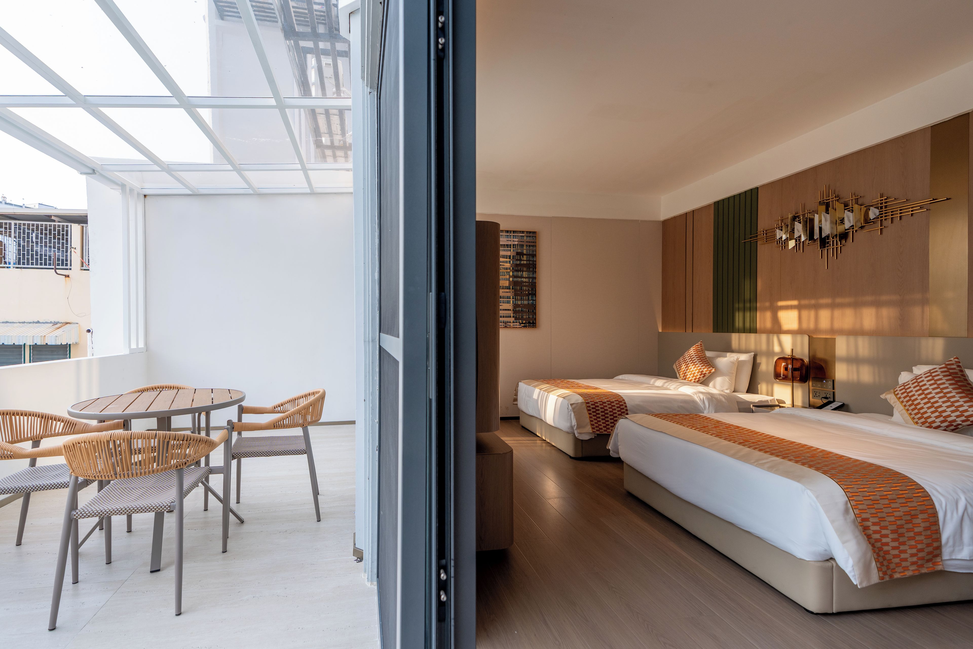 A hotel room with a balcony, a dining area with wicker furniture, and a bed with a patterned bedspread.