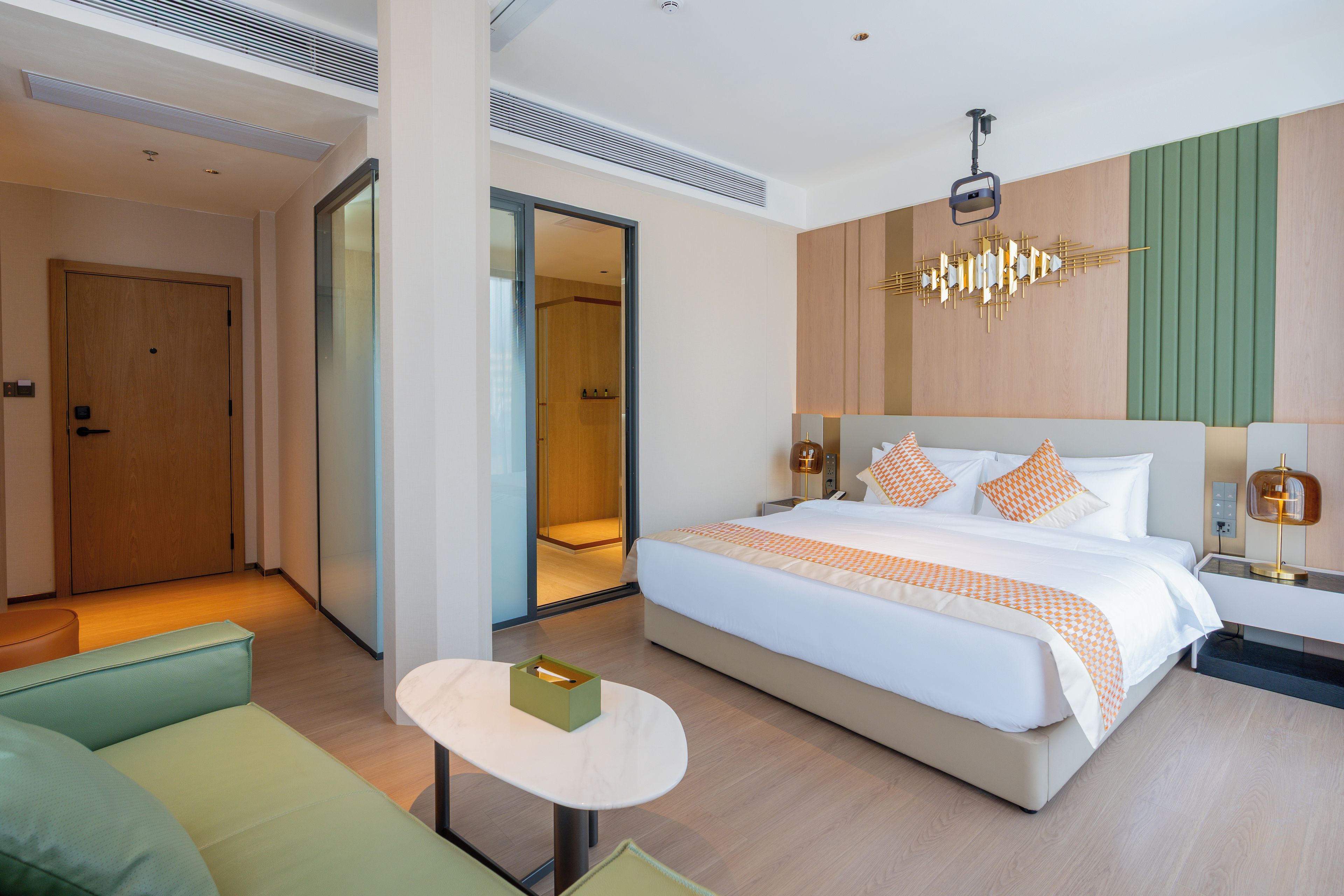 Ein modernes Hotelzimmer mit einem großen Bett, einem kleinen Tisch, einer Couch und einem durch eine Glastür einsehbaren Badezimmer.