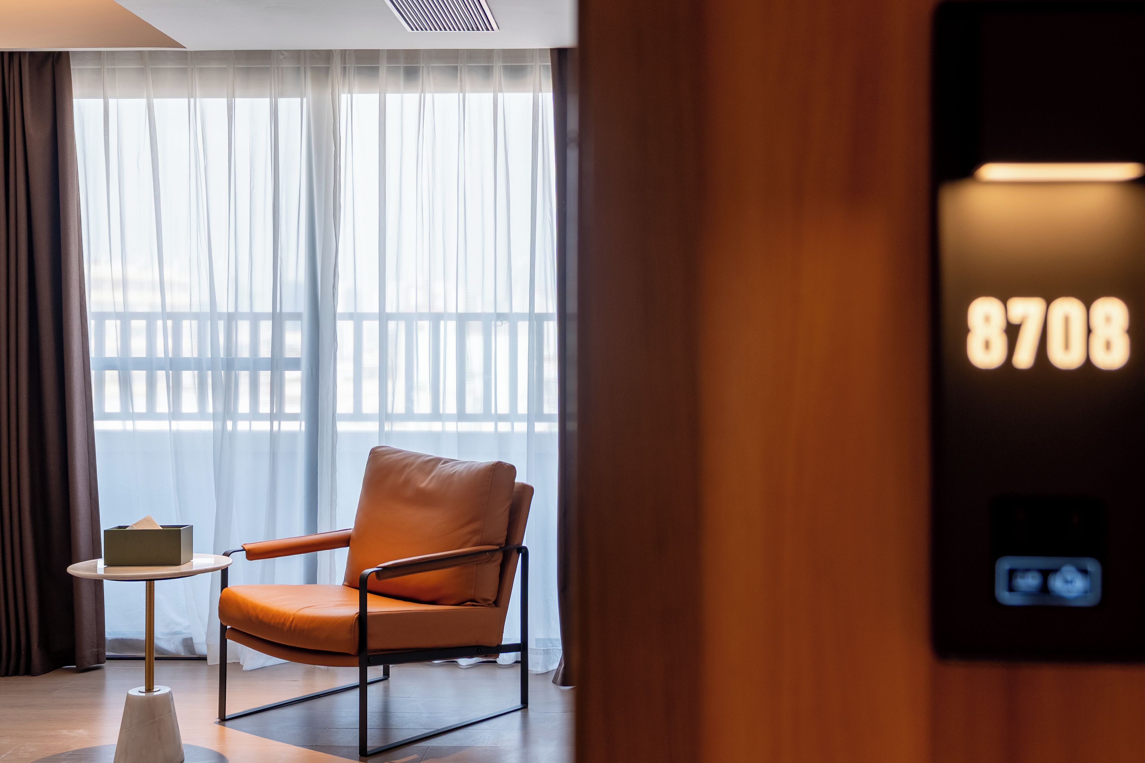 A hotel room with a leather chair, a small table, and a view of a balcony.