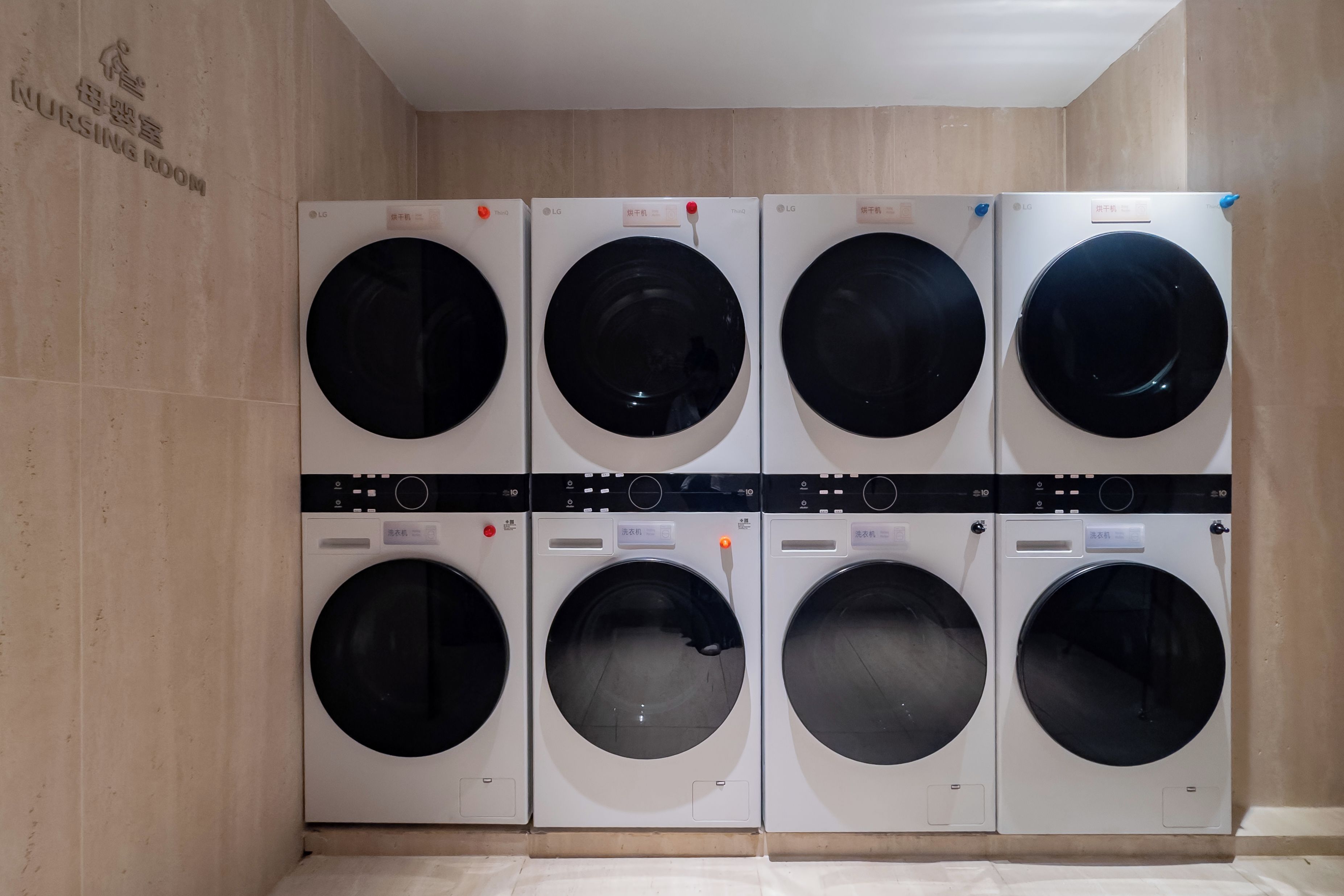 Una fila de seis lavadoras LG en un establecimiento, con un letrero que indica una sala de lactancia cerca.