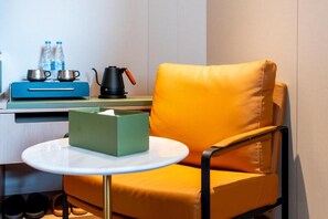 Een kleine kamer met een gele stoel, een tafel met zakdoosjes, een blauwe kast en een waterkoker.