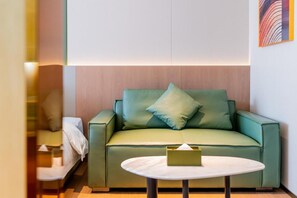 Een groene bank met een kussen, een klein rond tafeltje met een zakdoos er bovenop, en een wand van houten panelen.