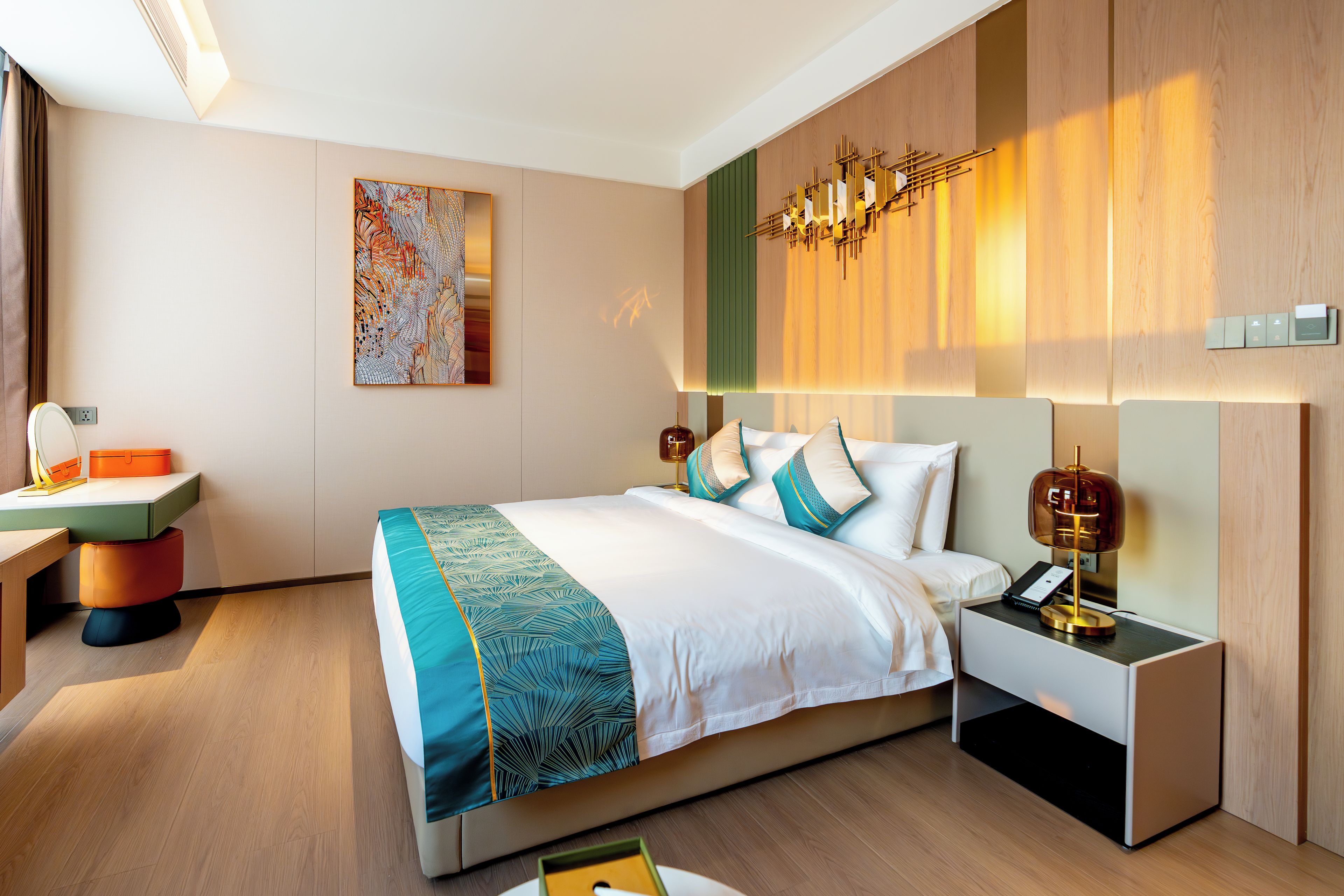 A modern hotel room with a large bed, bedside tables, a desk, and a painting on the wall.