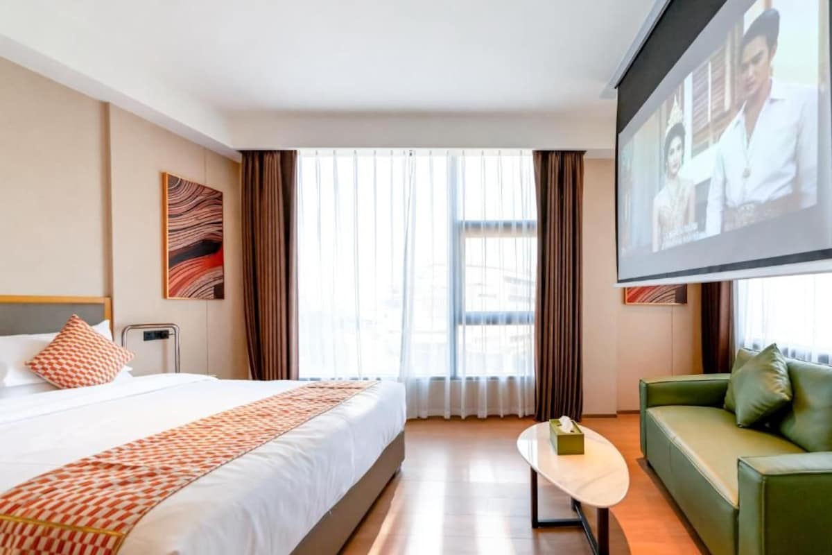Habitació d'hotel amb un llit, un sofà verd, una taula petita i un gran televisor.