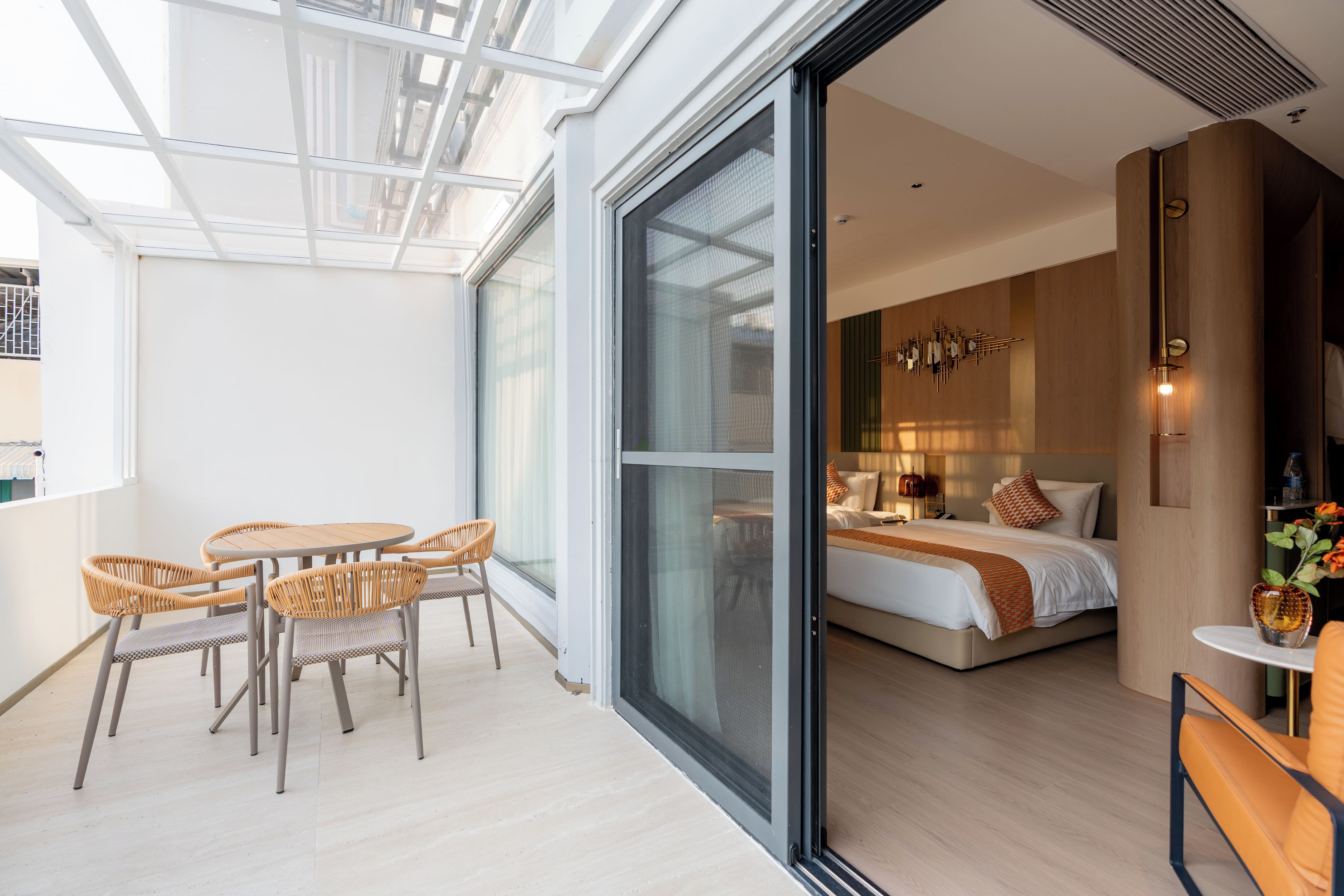 Ein modernes Hotelzimmer mit einer großen Schiebeglasdoor zu einem Balkon mit Korbmöbeln.