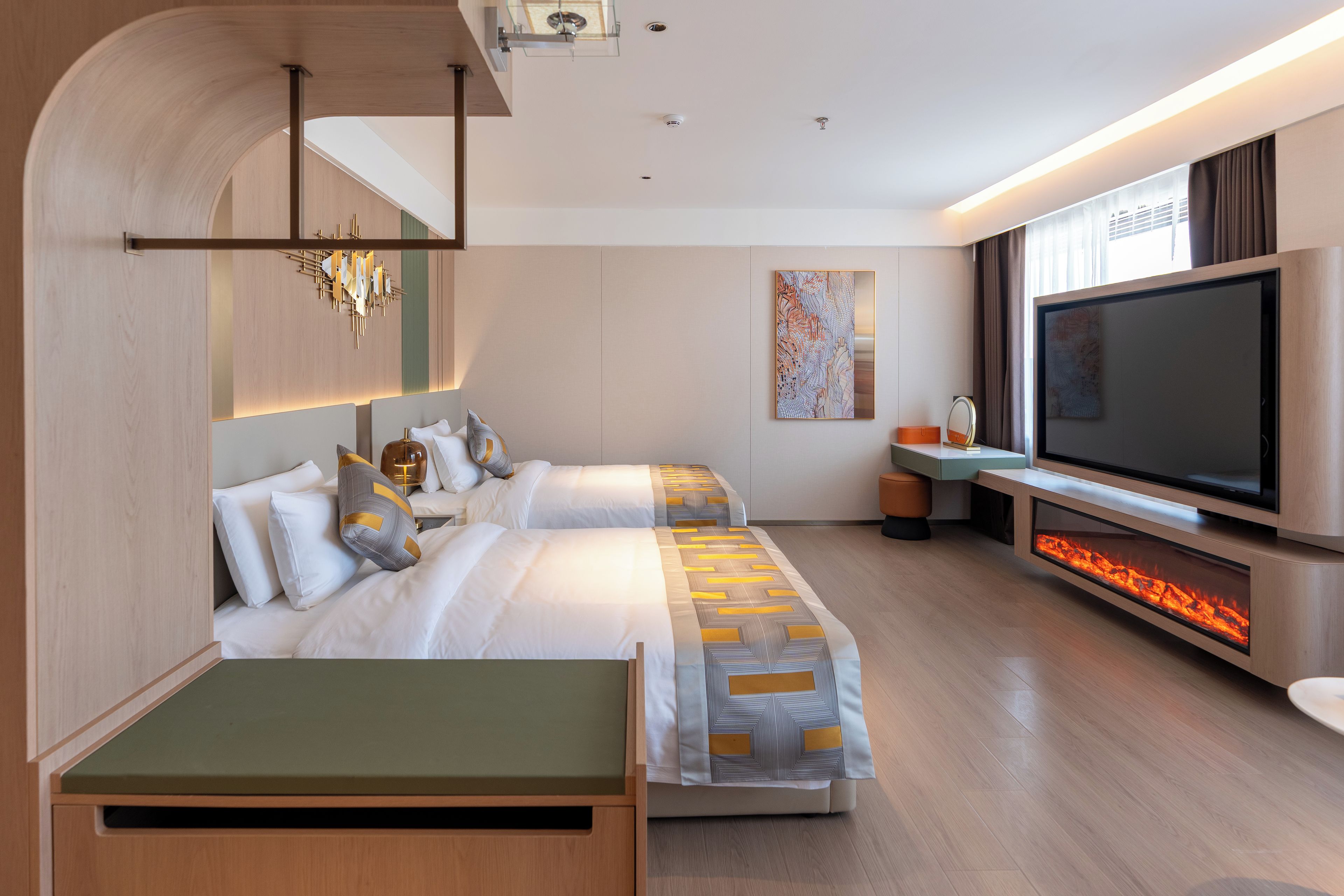 A modern hotel room with a large flat-screen TV, a fireplace, and a bed with multiple pillows.