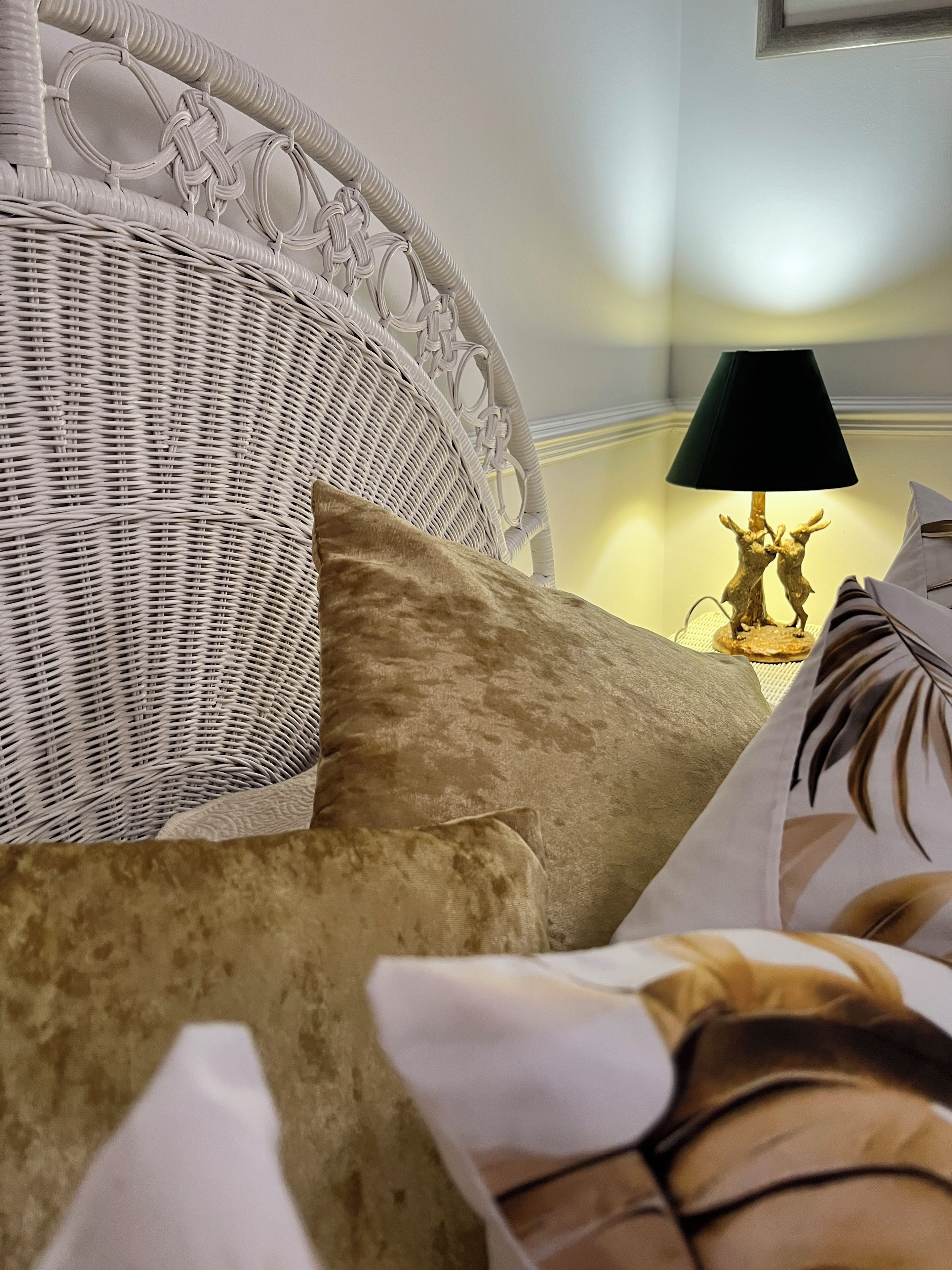 A wicker headboard with a lamp and decorative items on a bedside table.