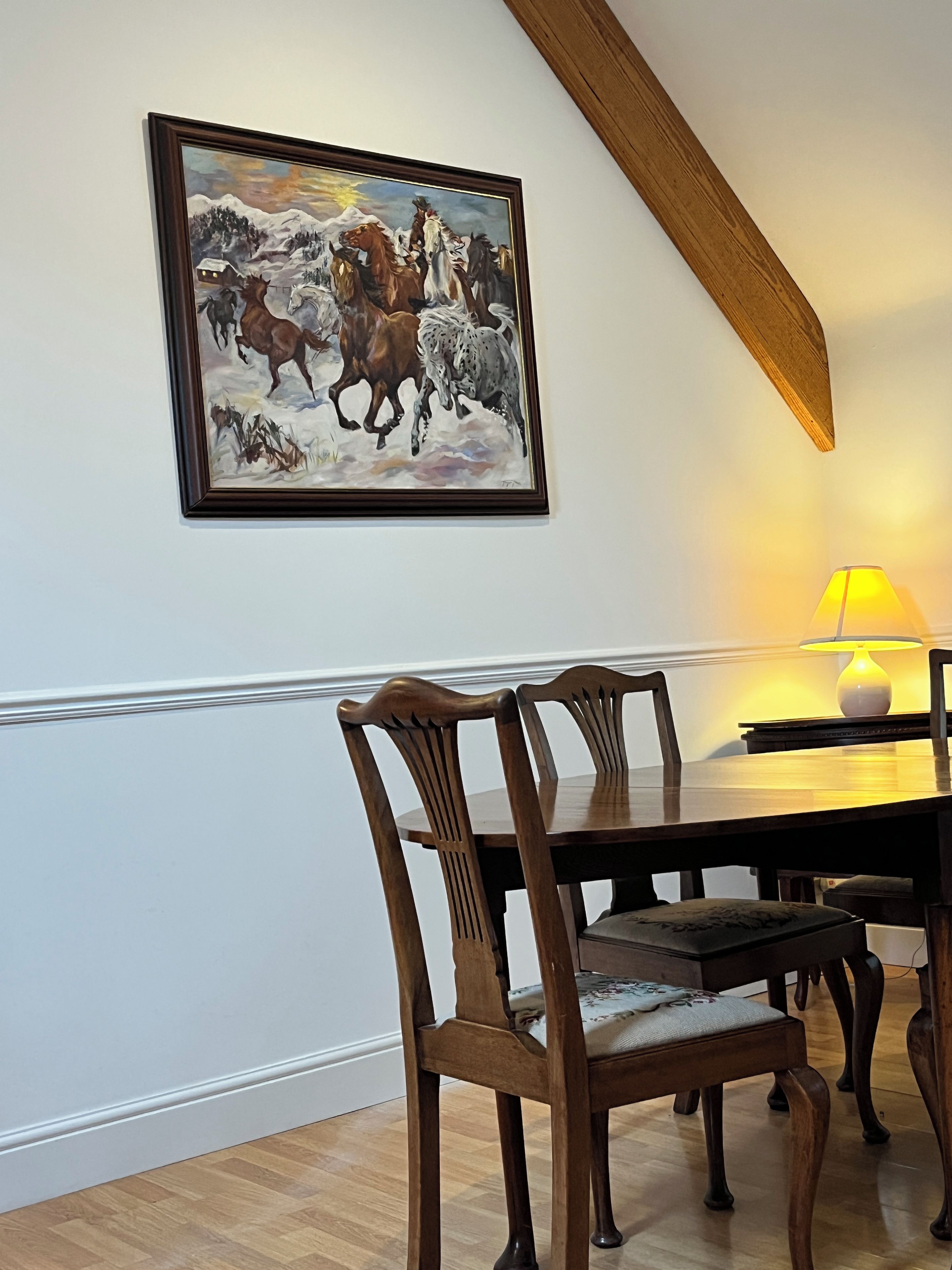 Een eetgedeelte met een houten tafel, stoelen en een schilderij van paarden aan de muur.