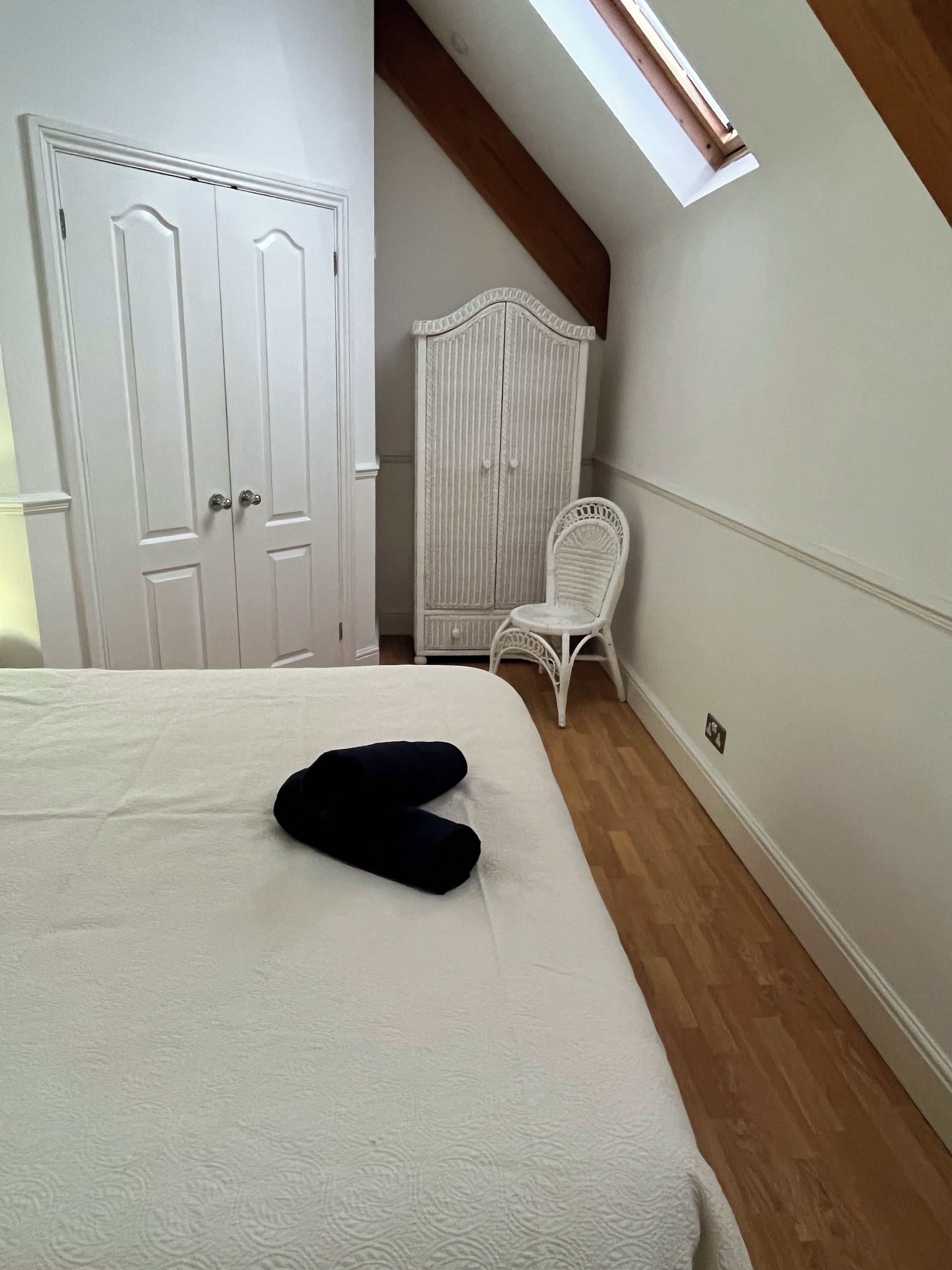 A bedroom with a bed, a wardrobe, a chair, and a skylight.