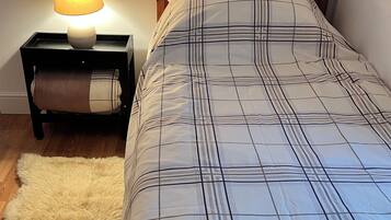 A bedroom with a wooden headboard, a bed with a plaid bedspread, a bedside lamp, a fluffy rug, and a nightstand with a lamp and a tissue box.