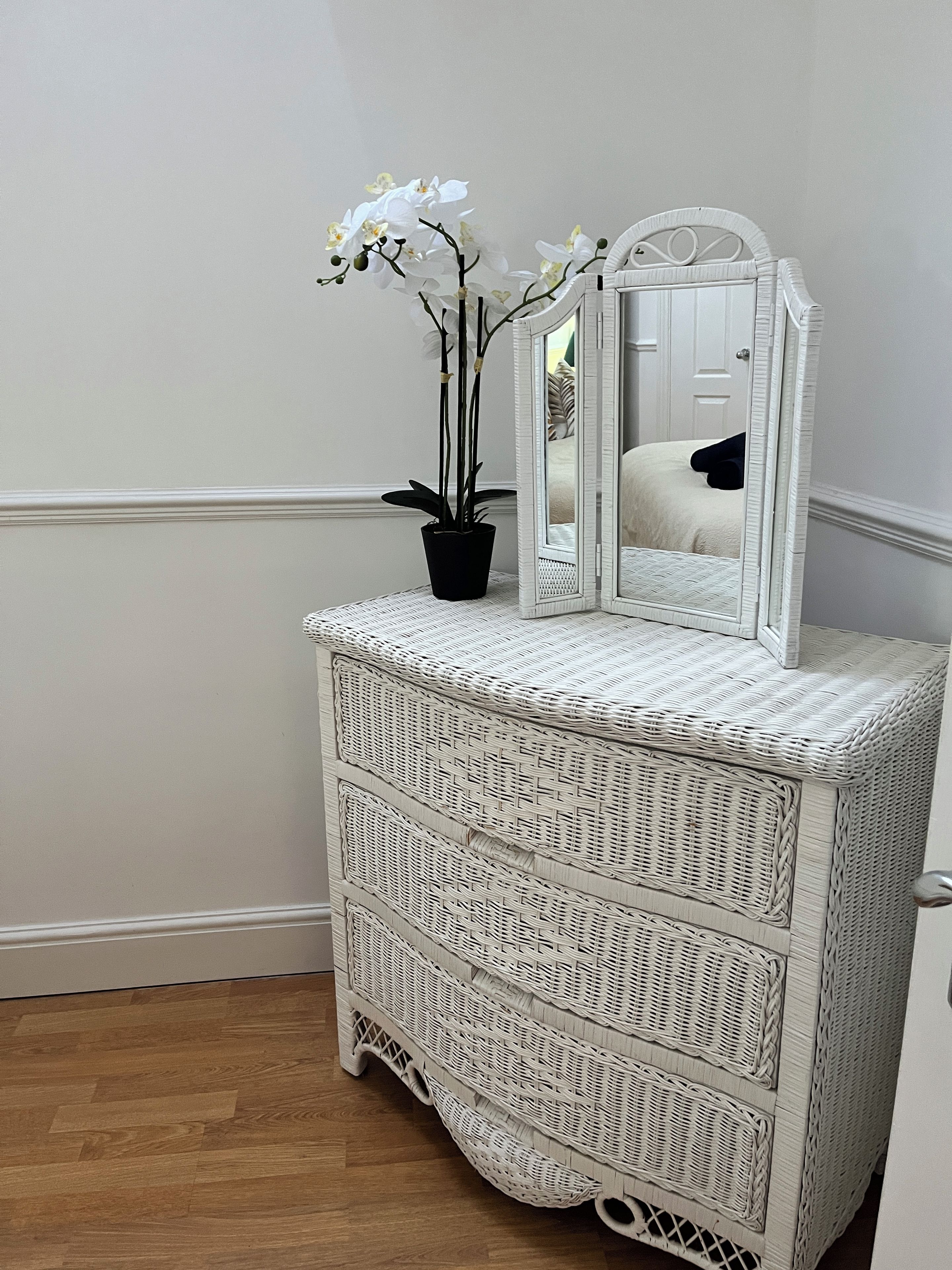 Een witte rieten dressoir met spiegel en een potorkidee.